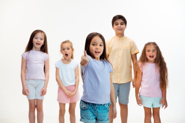 El retrato de niño y niñas felices lindos niños pequeños en ropa casual elegante mirando al frente contra la pared blanca del estudio