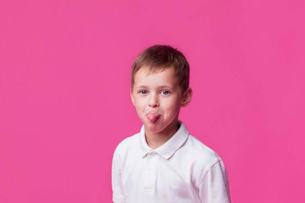 Retrato de niño niño sacando la lengua sobre fondo rosa