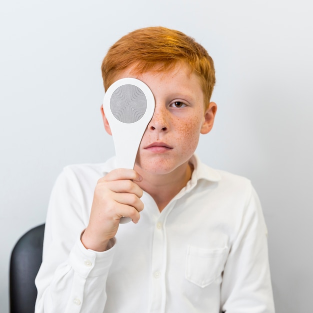 Retrato de niño con pecas sosteniendo oclusor delante de sus ojos