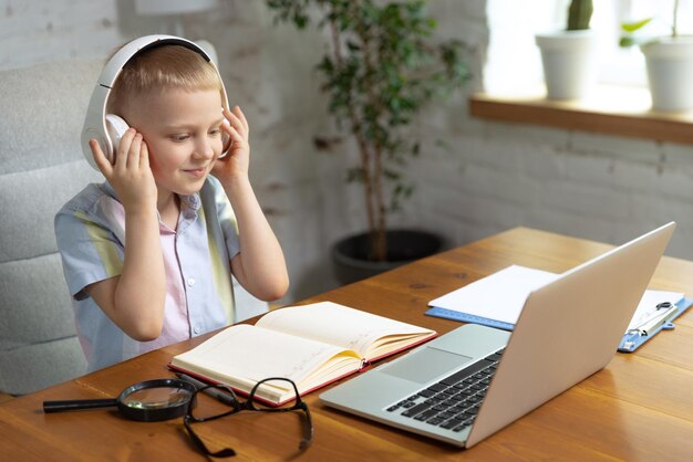 Retrato de niño pequeño con auriculares estudiando en casa mirando en una computadora portátil trabajando con el maestro Educación en línea