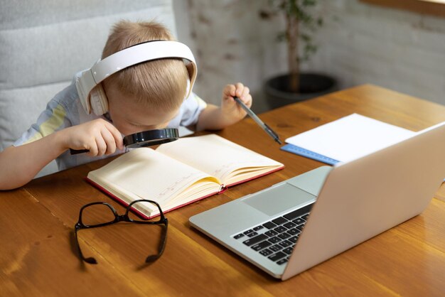 Retrato de niño pequeño en auriculares estudiando en casa mirando en la computadora portátil trabajando con el maestro Sintiéndose cansado