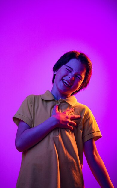 Retrato de niño pequeño en camiseta amarilla posando riendo aislado sobre fondo púrpura en neón