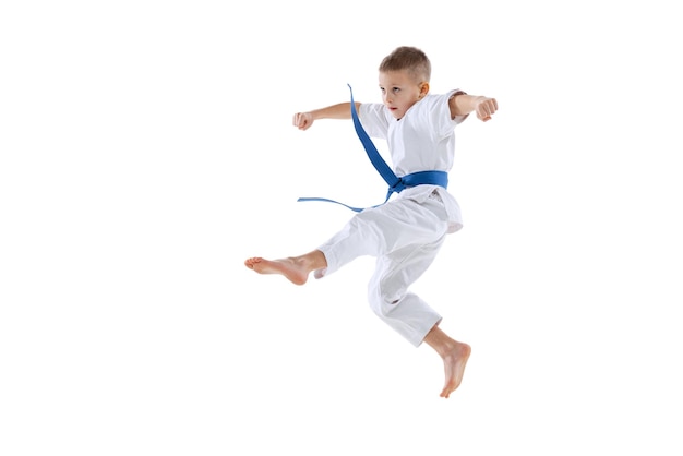 Retrato de niño pequeño en kimono con entrenamiento de cinturón azul aislado sobre fondo blanco de estudio