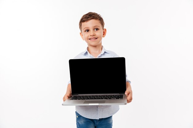 Retrato de un niño pequeño lindo que muestra la computadora portátil de la pantalla en blanco