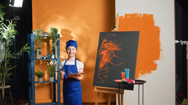 Retrato de un niño pequeño pintando un diseño artístico sobre lienzo, utilizando una paleta artística de aquarelle y un pincel. Niña aprendiendo a pintar obras maestras con acuarela y pincel, habilidades creativas.