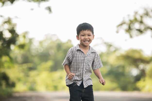 Retrato del niño pequeño que se coloca en el parque de naturaleza que sonríe a la cámara.