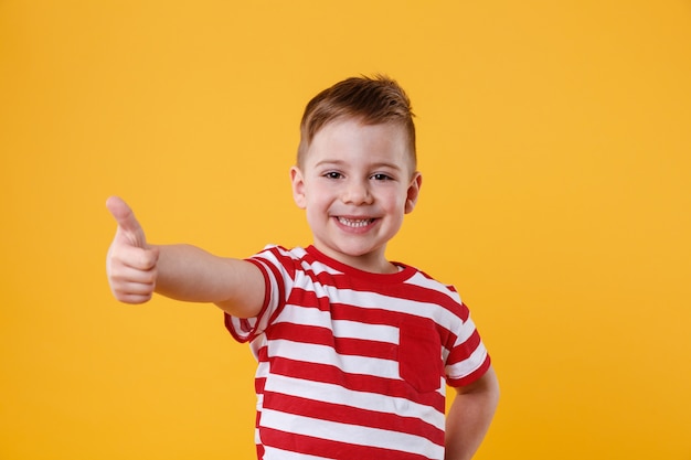 Retrato de un niño pequeño sonriente que muestra los pulgares para arriba