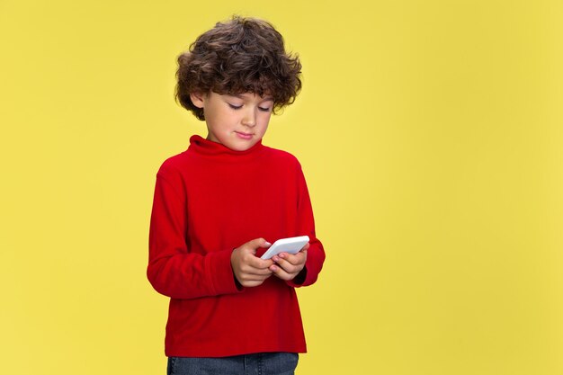 Foto gratuita retrato de niño rizado bastante joven en ropa roja sobre fondo amarillo de estudio. infancia, expresión, educación, concepto de diversión.