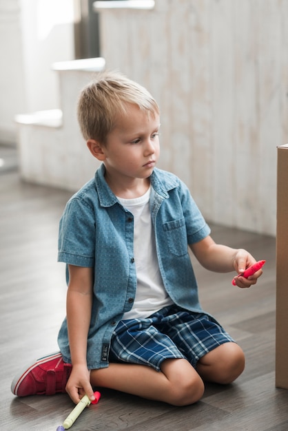 Retrato de un niño rubio dibujando con rotulador en caja de cartón