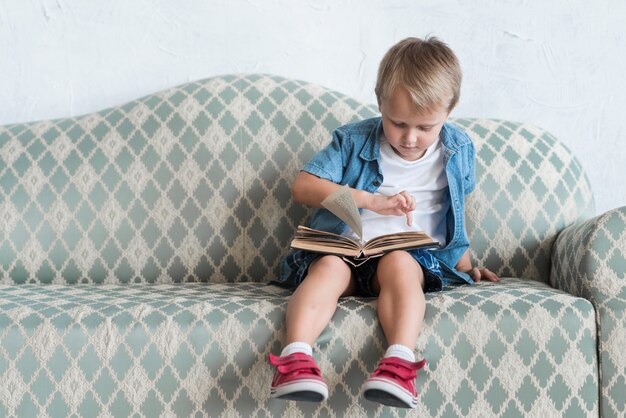 Retrato de un niño sentado en el sofá apuntando el dedo sobre el libro