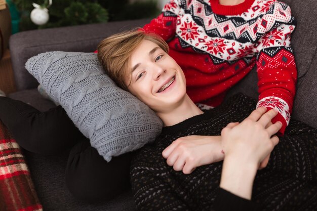 Retrato de un niño sonriente y genial acostado sobre una almohada mientras se apoya en las rodillas de una niña y mira felizmente a la cámara