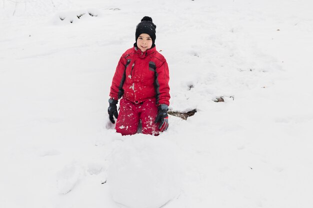 Retrato de un niño sonriente sentado en la tierra nevada mirando a cámara