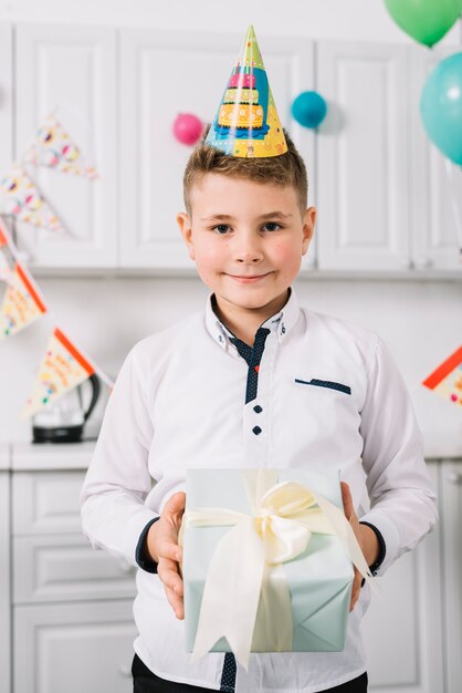 Retrato de un niño sonriente con sombrero de fiesta en la cabeza, sosteniendo la caja actual envuelta