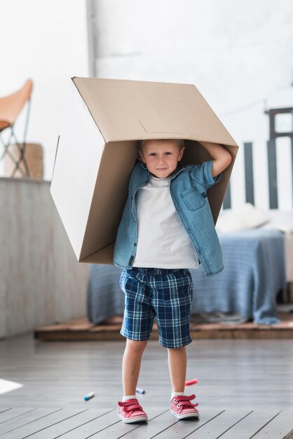 Retrato de un niño sosteniendo una caja de cartón sobre su cabeza en el dormitorio