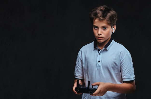 El retrato de un niño vestido con una camiseta blanca lleva un auricular inalámbrico que tiene un mando a distancia.