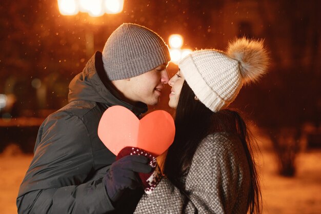 Retrato nocturno al aire libre de pareja joven con corazón de papel en la calle