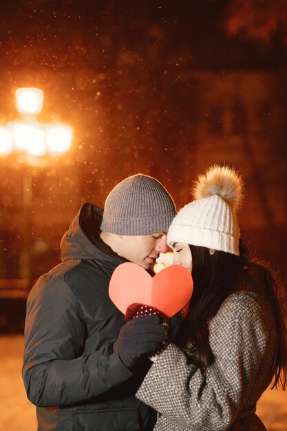 Retrato nocturno al aire libre de pareja joven con corazón de papel en la calle