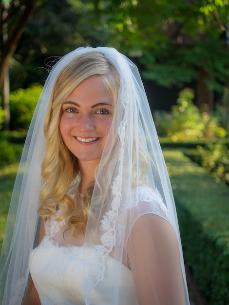 Retrato de una novia sonriente en un jardín rodeado de vegetación bajo la luz del sol