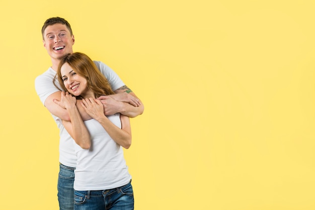 Retrato de un novio abrazando a su novia sonriente por detrás contra el fondo amarillo