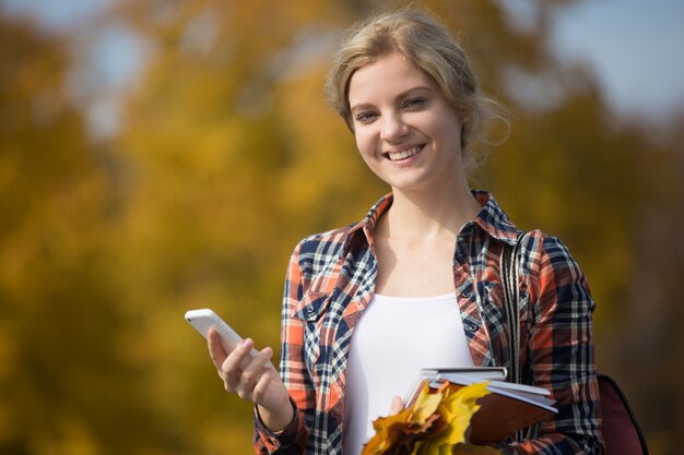 Retrato de los outsides del estudiante, sosteniendo el teléfono móvil en una mano