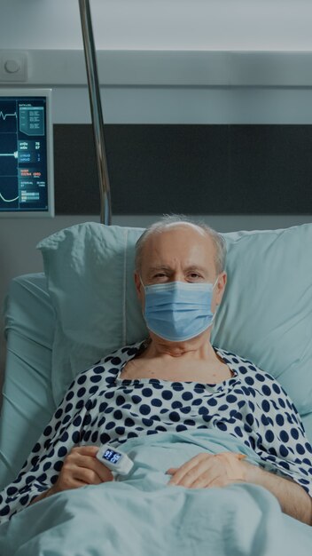 Retrato de paciente anciano con mascarilla sentado en la sala del hospital