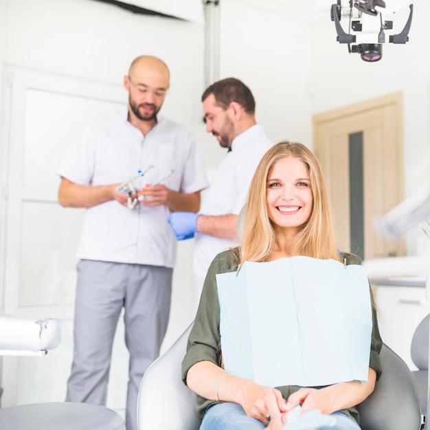 Retrato del paciente femenino feliz que se sienta delante de dos dentistas masculinos