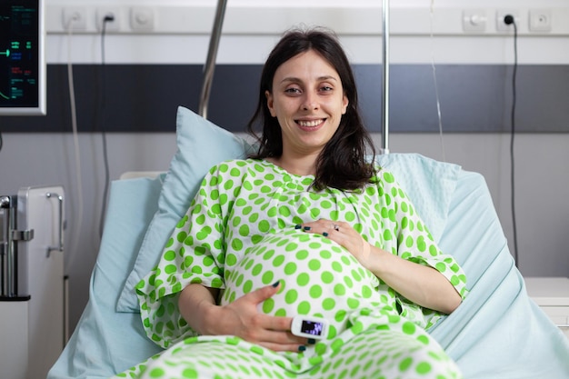 Foto gratuita retrato de una paciente sonriente con embarazo, esperando recibir un examen médico para comprobar su atención médica. mujer esperando un hijo y preparándose para dar a luz en la sala del hospital