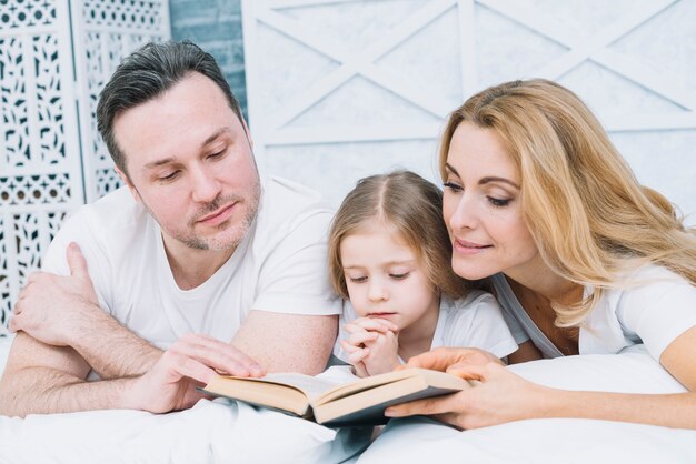 Retrato de padre madre e hija leyendo un libro en la cama