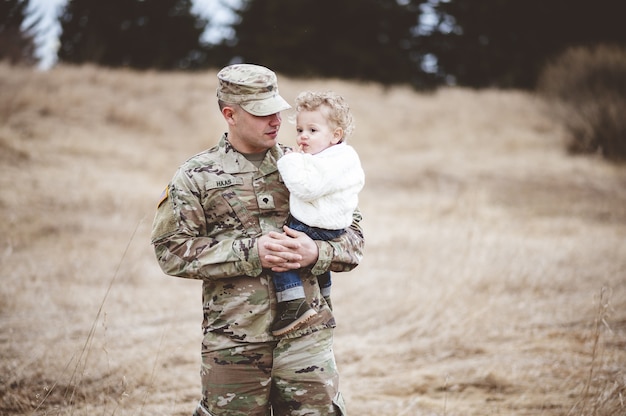 Foto gratuita retrato de un padre soldado sosteniendo a su hijo en un campo