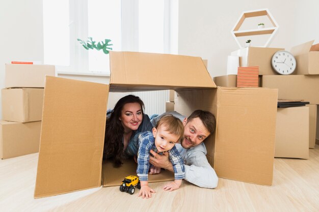 Retrato de unos padres felices jugando con un niño pequeño dentro de la caja de cartón