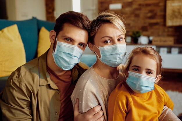 Retrato de padres sonrientes con su hija usando máscaras faciales en casa debido a la pandemia de COVID19