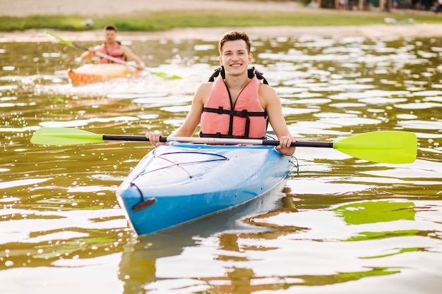 Retrato de paleta de explotación masculina flotando en kayak sobre el lago brillante
