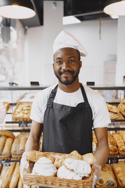 Retrato de panadero afroamericano con pan fresco en la panadería. Chef de repostería con pastelería pequeña.