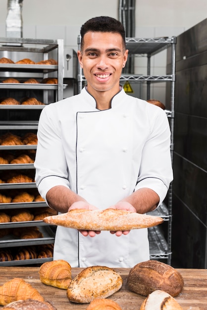 Retrato de un panadero de sexo masculino joven sonriente que sostiene el pan del baguette