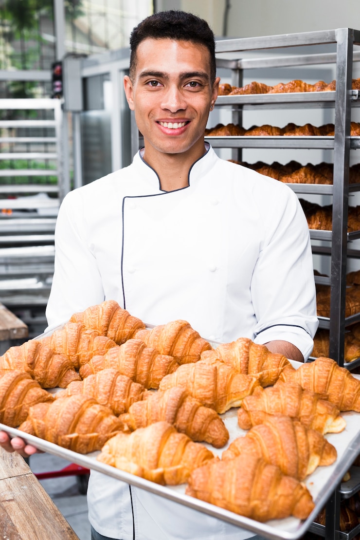 Foto gratuito retrato de un panadero de sexo masculino sonriente que sostiene la bandeja de croissant cocido