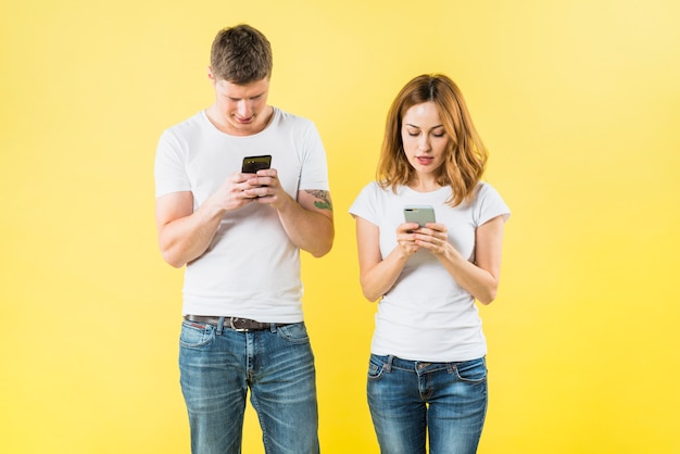 Retrato de un par joven que manda un SMS en el teléfono elegante contra el contexto amarillo