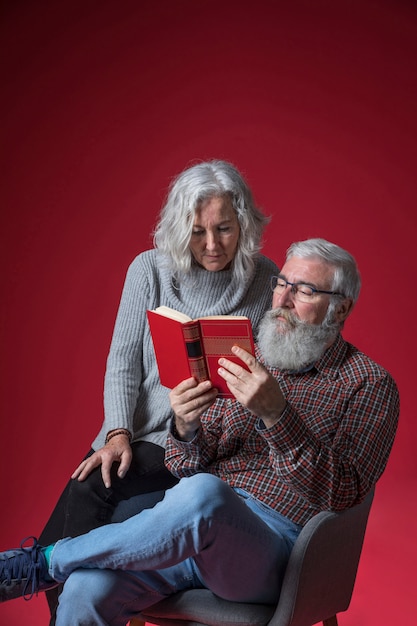 Retrato de un par mayor que lee el libro contra fondo rojo