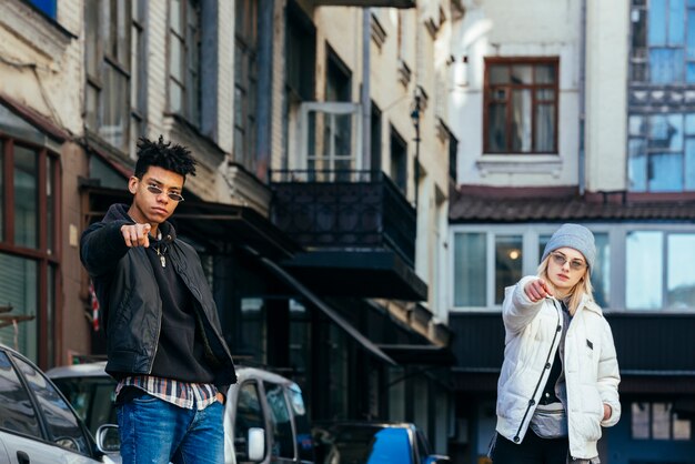 Retrato de pareja adolescente de moda apuntando sus dedos hacia la cámara