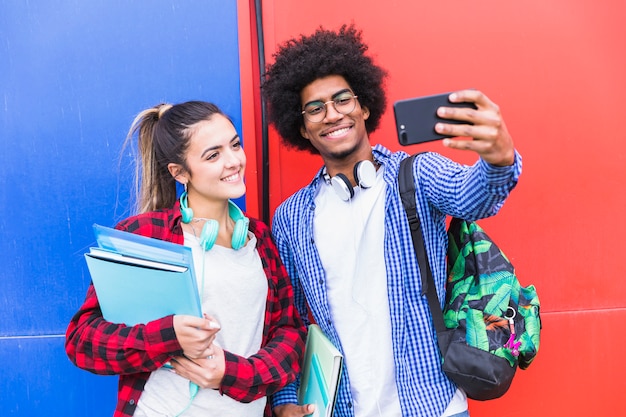 Retrato de una pareja adolescente sonriente tomando selfie juntos en un teléfono móvil contra una pared de color