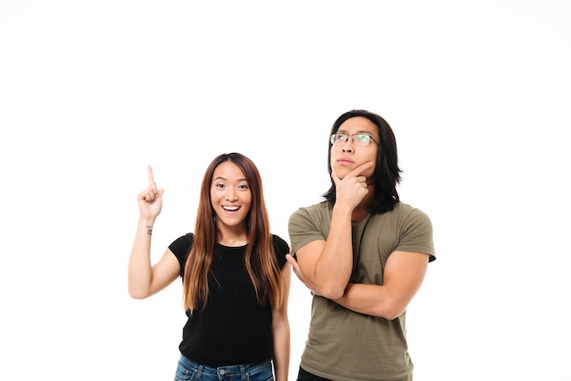 Retrato de una pareja asiática sonriente reflexiva que señala el dedo hacia arriba