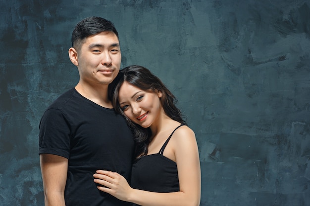 Retrato de pareja coreana sonriente en un estudio gris