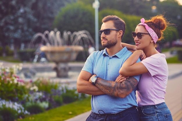 Retrato de una pareja elegante sobre una fuente de la ciudad. Un hombre con tatuajes en los brazos cuelga a una mujer pelirroja.