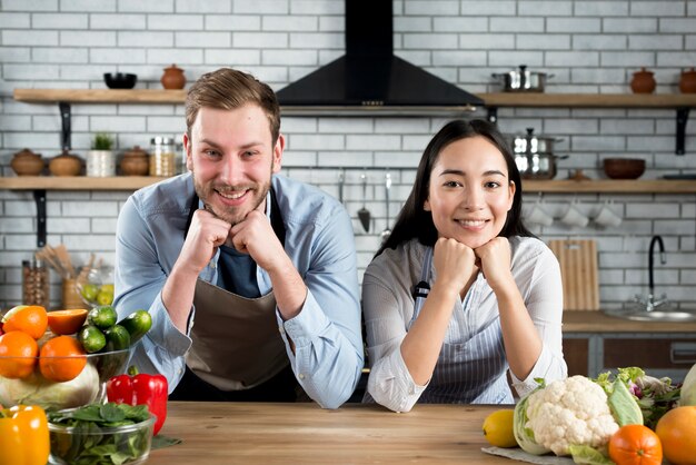 Retrato de pareja feliz mirando a la cámara en su cocina moderna con delantal