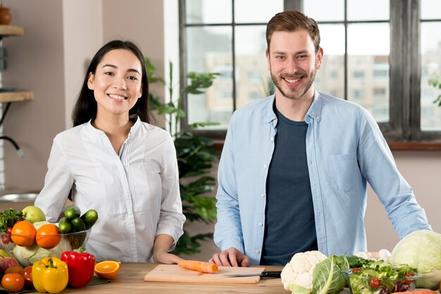 Retrato de una pareja feliz de pie detrás del mostrador de la cocina con diferentes tipos de vegetales