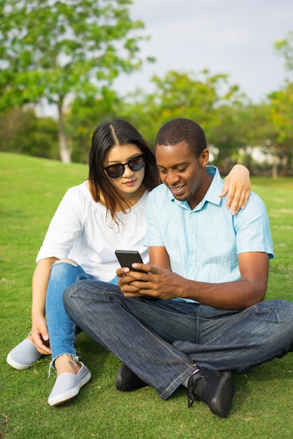 Retrato de pareja feliz viendo fotos en teléfono inteligente en el parque.