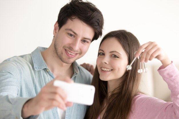 Retrato de una pareja hermosa haciendo selfie en móvil sosteniendo la llave