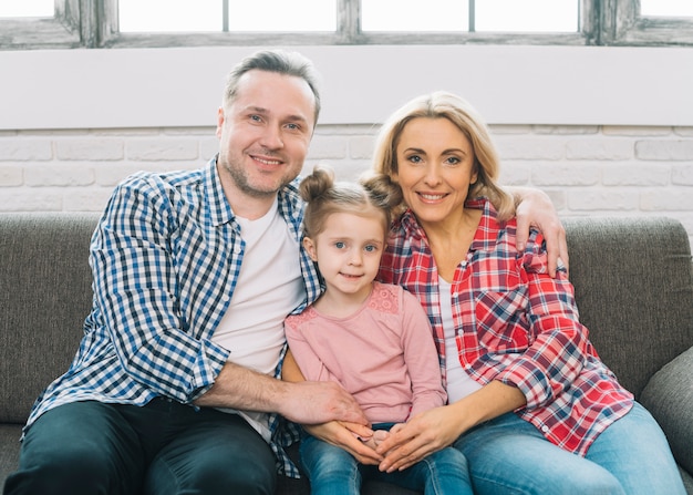 Retrato de la pareja y de la hija jovenes sonrientes que se sientan en el sofá