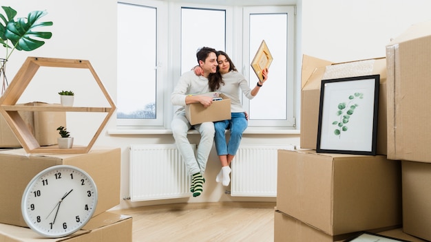 Foto gratuita retrato de una pareja joven amorosa sentada en el alféizar de la ventana en un nuevo apartamento mirando el marco