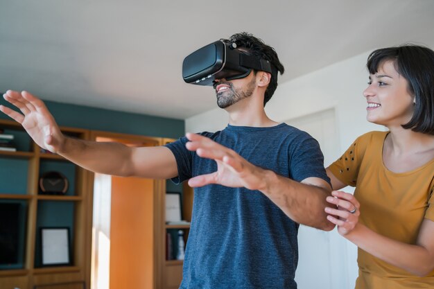 Retrato de pareja joven divirtiéndose juntos y jugando videojuegos con gafas VR mientras se queda en casa. Nuevo concepto de estilo de vida normal.