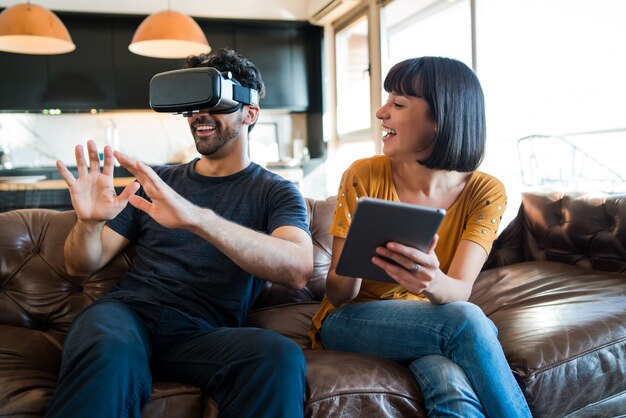 Retrato de pareja joven divirtiéndose juntos y jugando videojuegos con gafas VR mientras se queda en casa